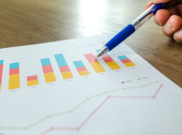 A Hand Holding A Pen Points To A Graph On Paper
