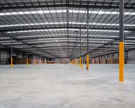 A spacious warehouse featuring concrete floors and prominent yellow support poles throughout the interior