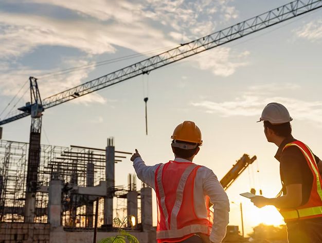 Two Construction Workers Pose In Front Of A Construction Site