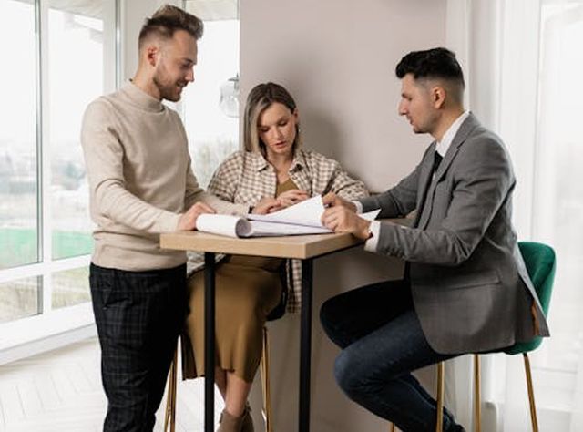 Three Colleagues At A Table, Analyzing Documents And Collaborating On A Project