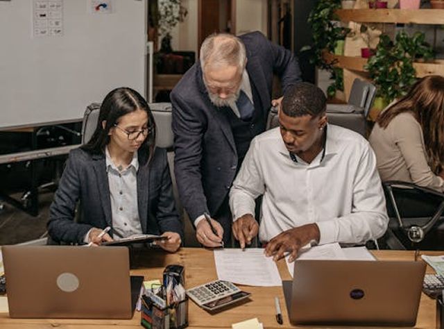 Three Individuals Collaborating On Paperwork At A Desk