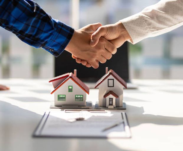 Two Individuals Shaking Hands Over A Small House Model