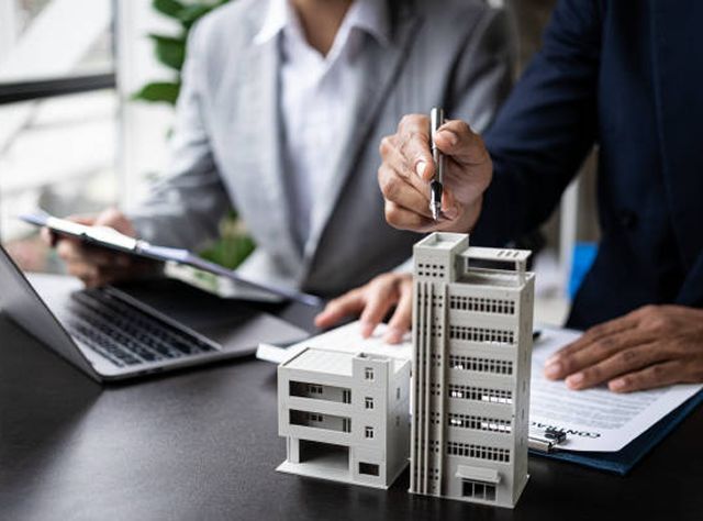 Two Professionals In Business Attire Examine A Building Model